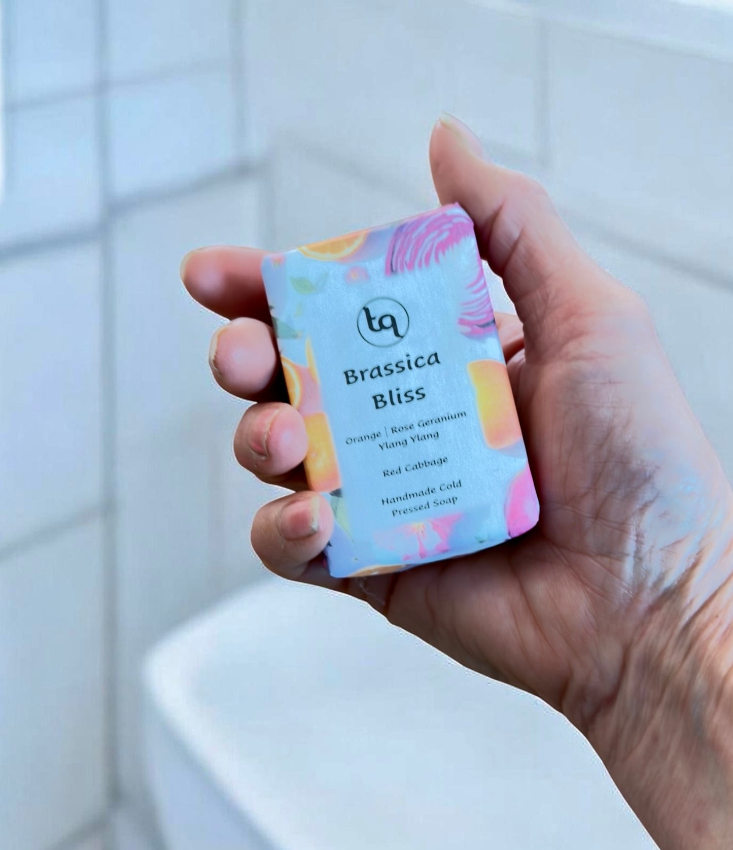 Hand holding a Truequest soap bar with colorful packaging against a tiled bathroom background