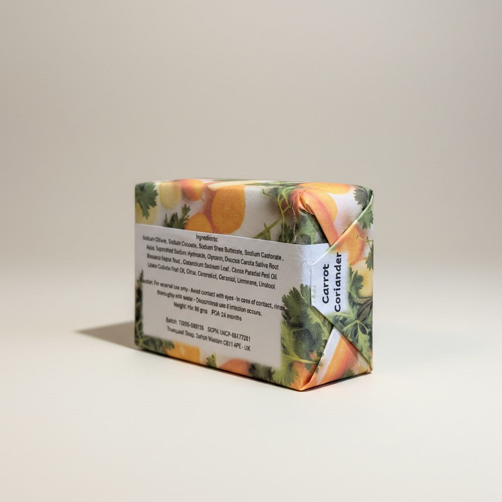 The reverse view of a paper-wrapped Truequest carrot and coriander cold-pressed soap bar, highlighting the back packaging label where the ingredients list is clearly legible