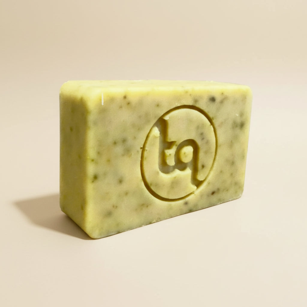 A front view of an unwrapped Truequest carrot and coriander cold-pressed soap bar, displaying its natural color, rustic texture, and the crisp TQ logo stamped into the center