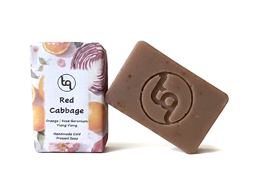 A product photo of two Truequest red cabbage cold-pressed soap bars, featuring one bar neatly enclosed in its paper packaging and a second naked bar revealing its unique natural colour.