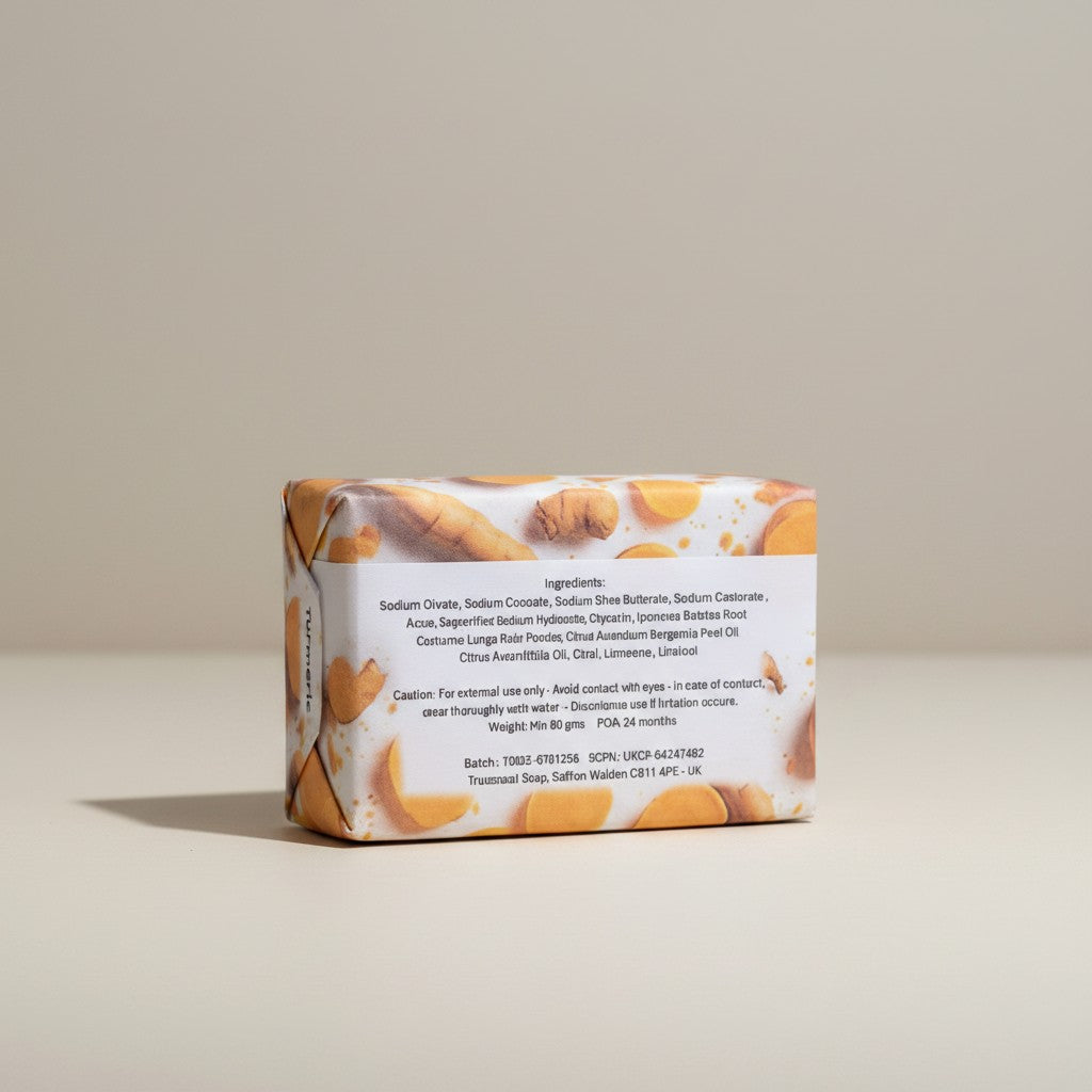 The reverse view of a paper-wrapped Truequest turmeric cold-pressed soap bar, highlighting the back packaging label where the ingredients list is clearly legible