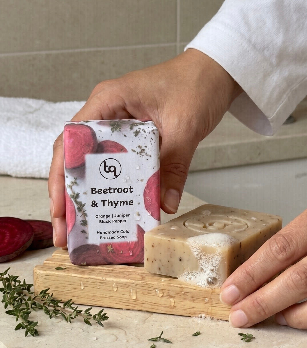 Hand holding a bar of Truequest Beetroot and Thyme soap with on a wooden stand.