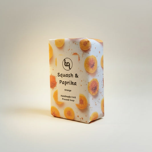 A rectangular bar of Truequest cold-pressed soap infused with squash and paprika. The soap has a natural, textured top surface and a rich, warm orange-brown color, photographed as the main product shot