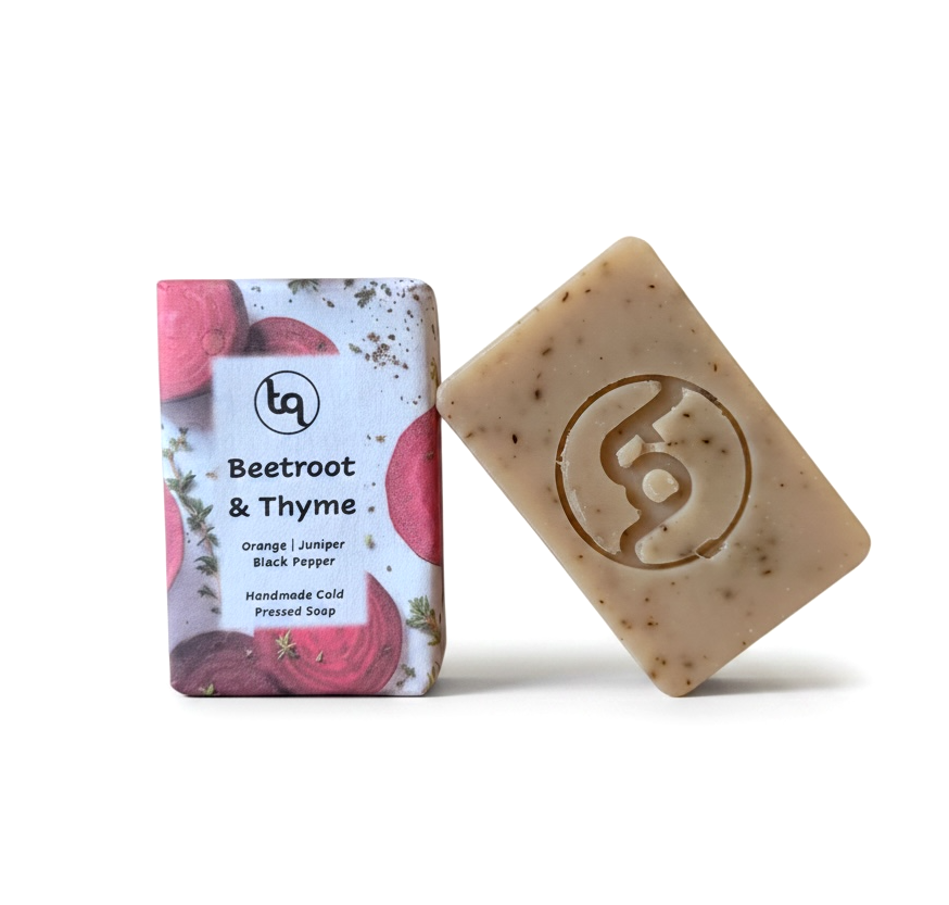 A product photo of two Truequest beetroot and thyme cold-pressed soap bars, featuring one bar neatly enclosed in its paper wrapper and a second naked bar