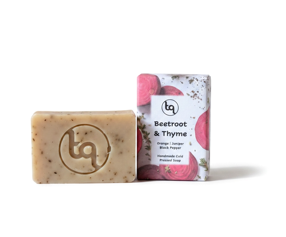 A product photo of two Truequest beetroot and thyme cold-pressed soap bars, featuring one bar neatly enclosed in its paper wrapper and a second naked bar