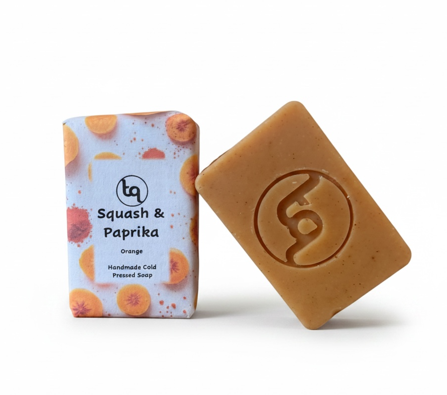 A side-by-side display of two Truequest squash and paprika cold-pressed soap bars: one fully wrapped in its paper packaging and the other bare to showcase its rich, earthy orange color and rustic texture.