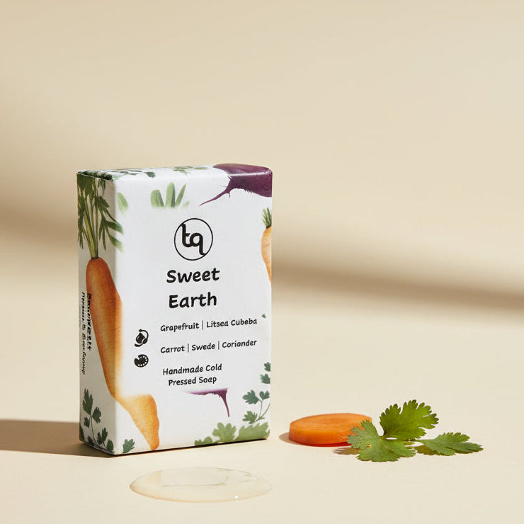 Carrot, coriander and swede 'Sweet Earth' soap packaging with a bar of soap and slices of carrot and coriander leaves on a beige background
