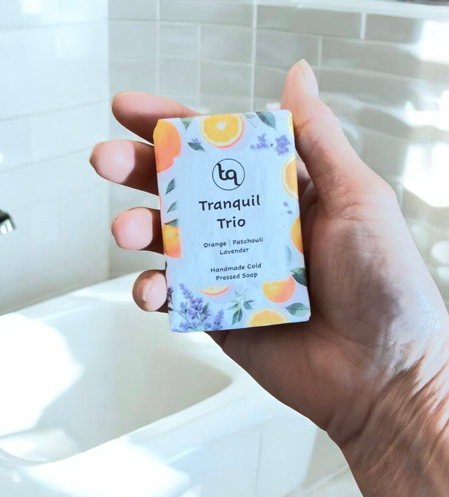 Hand holding a bar of Truequest soap labeled 'Tranquil Trio' with a tiled bathroom background