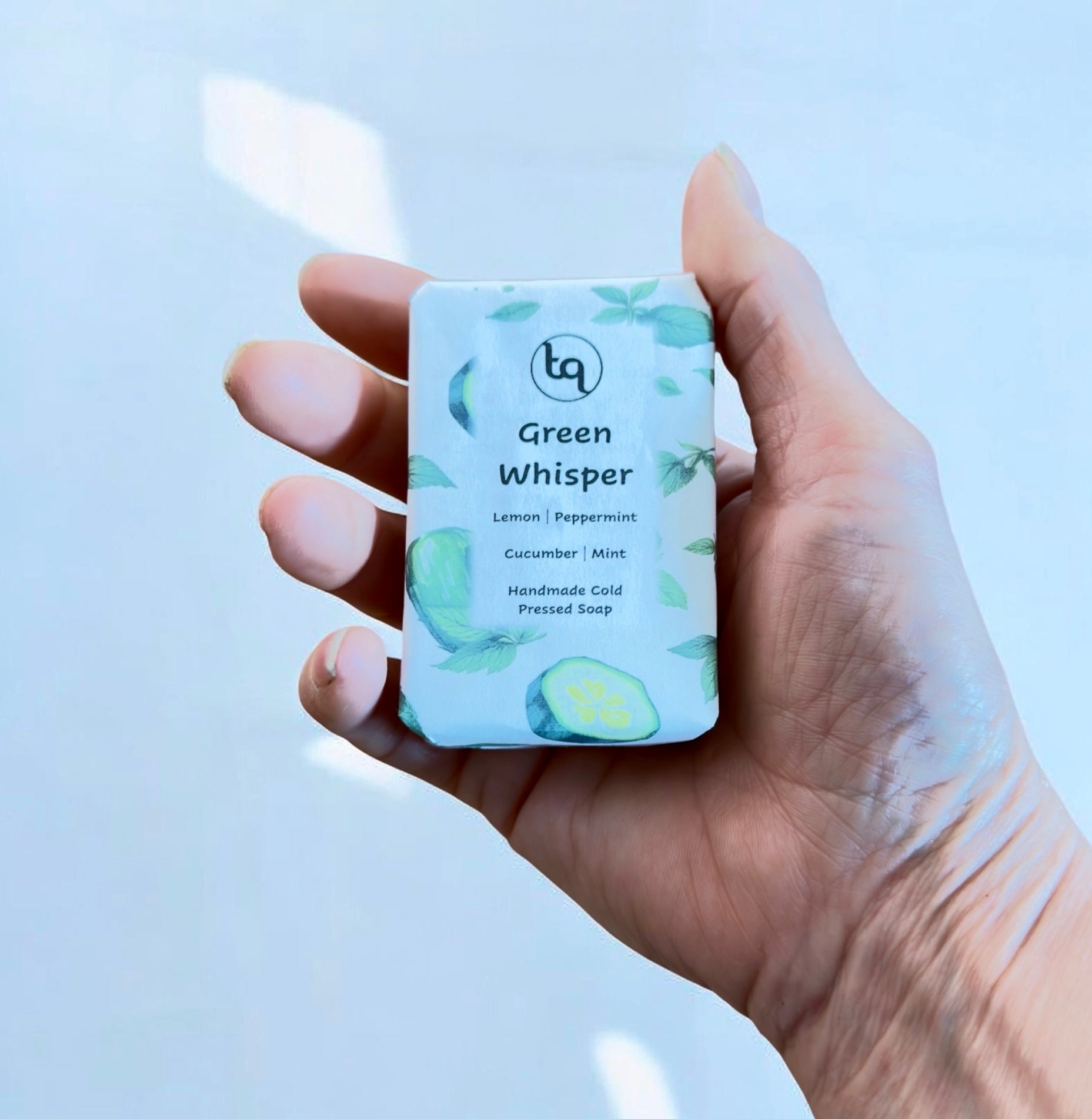 Hand holding a bar of Truequest cucumber and mint soap labeled 'Green Whisper' with a light background