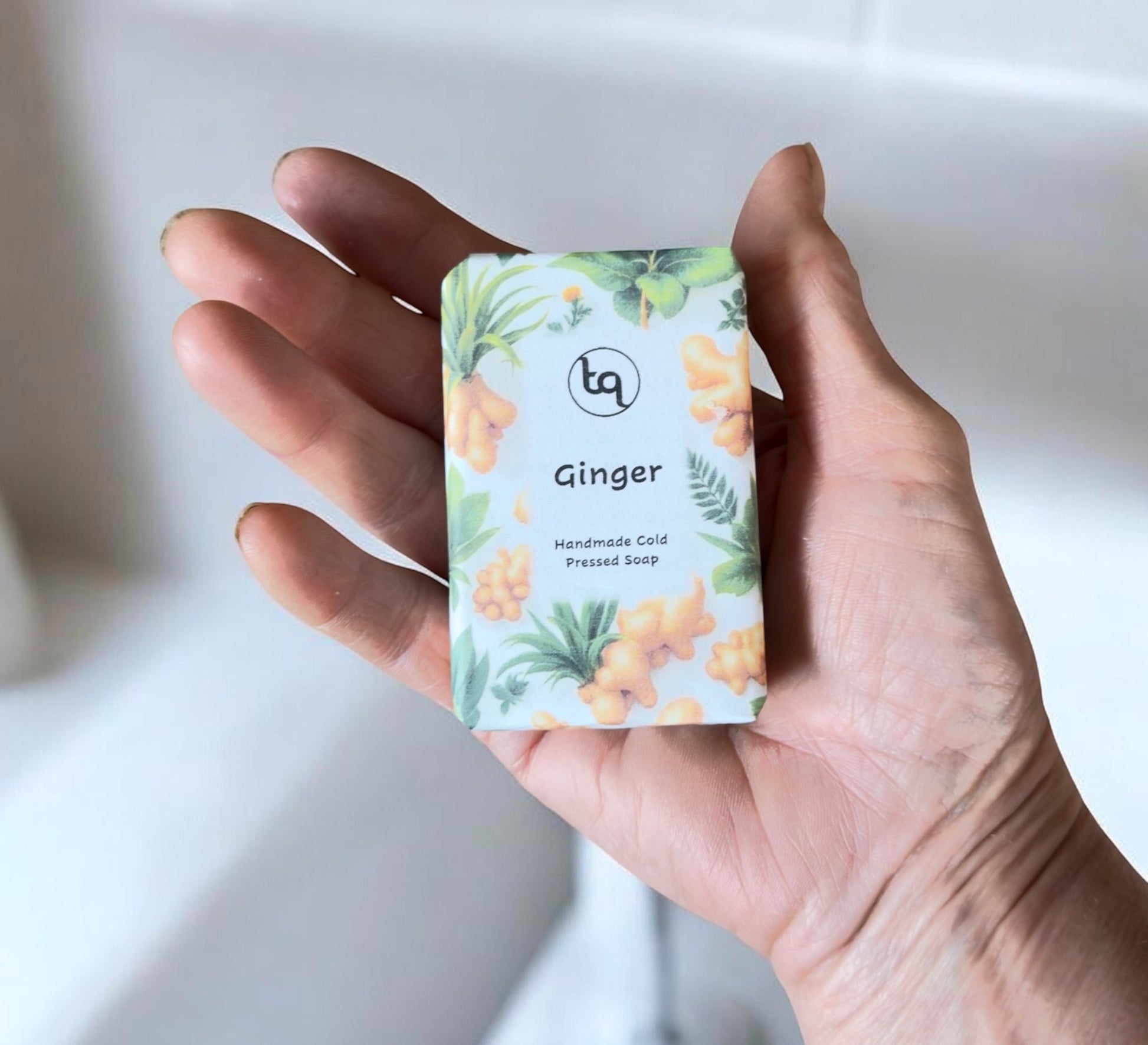 Handmade cold‑pressed ginger soap bar wrapped in botanical packaging in palm of hand for size indication from TrueQuest Soap.