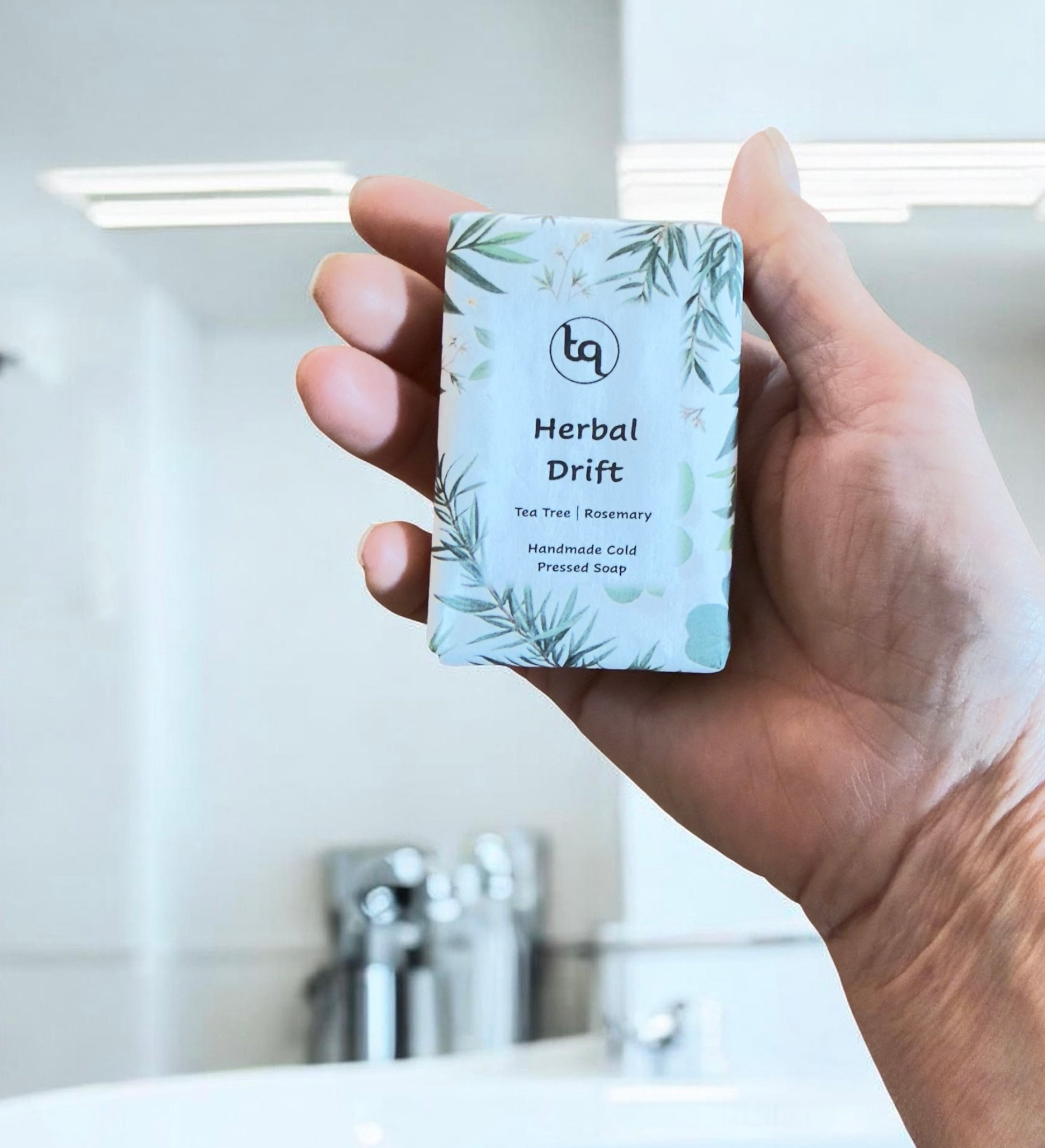 Hand holding a Truequest Herbal Drift cold pressed soap wrapped in green mint leaf patterned paper.