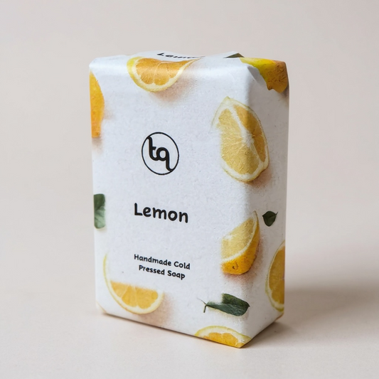 Lemon‑themed Truequest cold‑pressed soap wrapped in white paper decorated with citrus slices and green leaves.