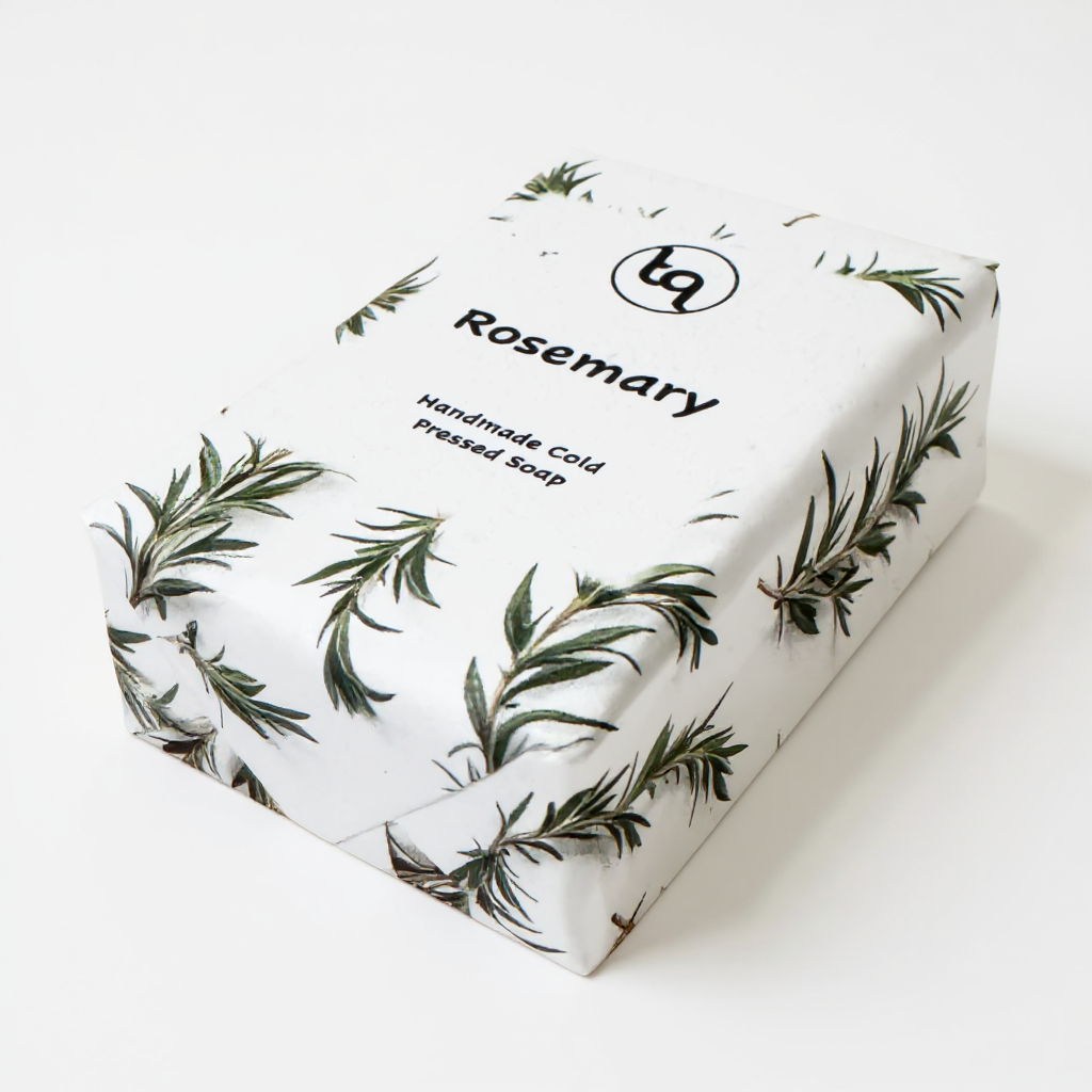 Front view of handmade cold‑pressed rosemary soap wrapped in white paper with green sprigs from Truequest Soap.