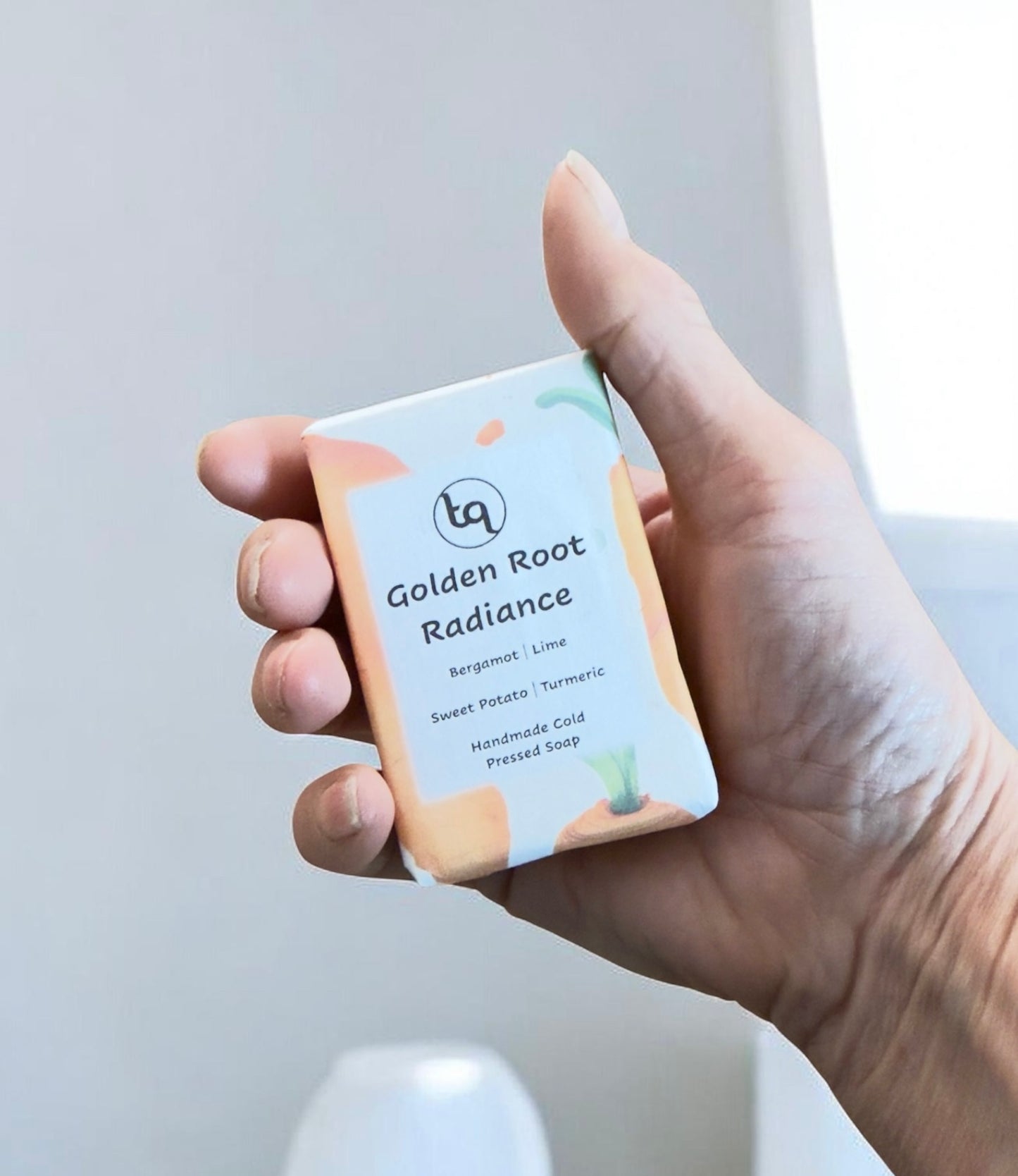 Hand holding a bar of Truequest soap labeled 'Golden Root Radiance' with a neutral background